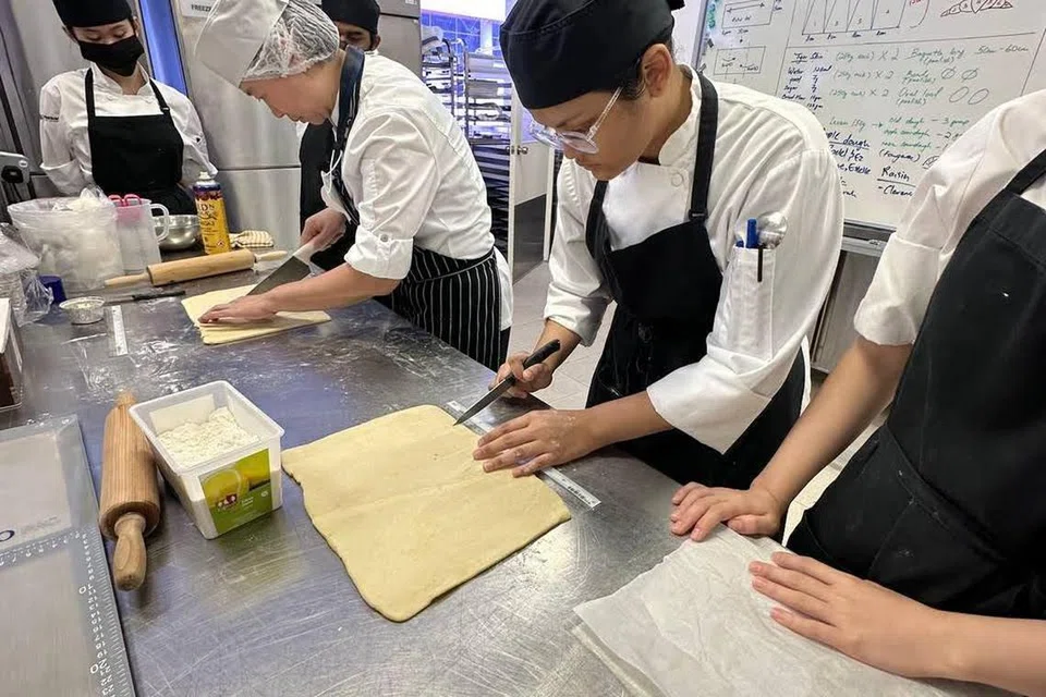 SELOK-BELOK KULINARI: Cik Fatin Aishah Hirwanis (dua dari kanan), lulusan Diploma dalam Perniagaan Makanan dan Minuman dengan Merit, semasa sesi latihan menyediakan pastri di sekolah.