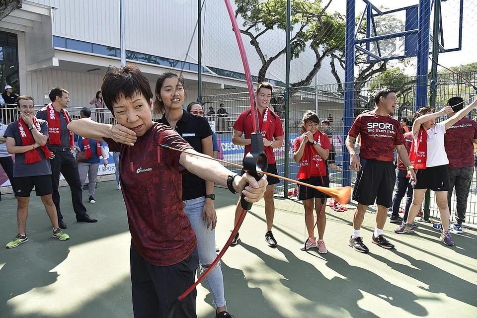 TUNJUK BAKAT MEMANAH: Cik Grace Fu (depan) mencuba sukan memanah sewaktu menyertai hari sukan dan senaman bersama kakitangan Decathlon dan SportSG di Decathlon Singapore Lab semalam. - Foto CMG