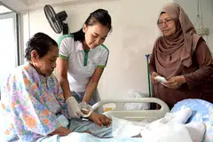 SELESA DENGAN MISI: Jururawat Berdaftar Kanan Siti Norbaya (tengah) menukar pembalut luka Cik Sameah Nahuwam, 85 tahun, sambil diperhatikan anak bongsu Cik Sameah, Cik Rohani Abu Bakri, 43 tahun. Cik Siti Norbaya turut mengajar cara menukar pembalut luka kepada penjaga pesakitnya agar mereka juga boleh melakukan hal tersebut jika perlu. - Foto KHALID BABA