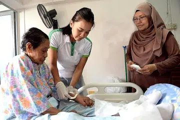 SELESA DENGAN MISI: Jururawat Berdaftar Kanan Siti Norbaya (tengah) menukar pembalut luka Cik Sameah Nahuwam, 85 tahun, sambil diperhatikan anak bongsu Cik Sameah, Cik Rohani Abu Bakri, 43 tahun. Cik Siti Norbaya turut mengajar cara menukar pembalut luka kepada penjaga pesakitnya agar mereka juga boleh melakukan hal tersebut jika perlu. - Foto KHALID BABA
