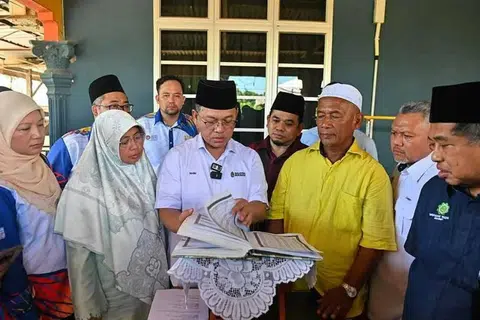 Menteri di Jabatan Perdana Menteri (Hal Ehwal Agama), Datuk Dr Mohd Na’im Mokhtar (tengah) melihat naskhah al-Quran tulisan tangan Allahyarhamah Nurly Sahirah semasa menziarahi rumah penuntut UPSI itu yang terkorban dalam nahas bas membawa pelajar UPSI di Gerik pada awal Jun lalu di Tanah Perkuburan Islam Kampung Gong Pasir, Kerandang.