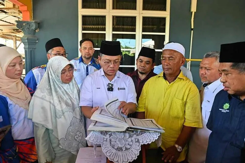 Menteri di Jabatan Perdana Menteri (Hal Ehwal Agama), Datuk Dr Mohd Na’im Mokhtar (tengah) melihat naskhah al-Quran tulisan tangan Allahyarhamah Nurly Sahirah semasa menziarahi rumah penuntut UPSI itu yang terkorban dalam nahas bas membawa pelajar UPSI di Gerik pada awal Jun lalu di Tanah Perkuburan Islam Kampung Gong Pasir, Kerandang.