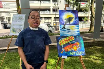 SUARA SENI: Muhammad Ridhwan Masli, 19 tahun, bersama salah satu hasil lukisannya yang dipamerkan di Pameran Seni Masyarakat SG60 di Tasik Guilin, Bukit Gombak pada 10 Ogos, sempena ulang tahun kemerdekaan ke-60 Singapura. 