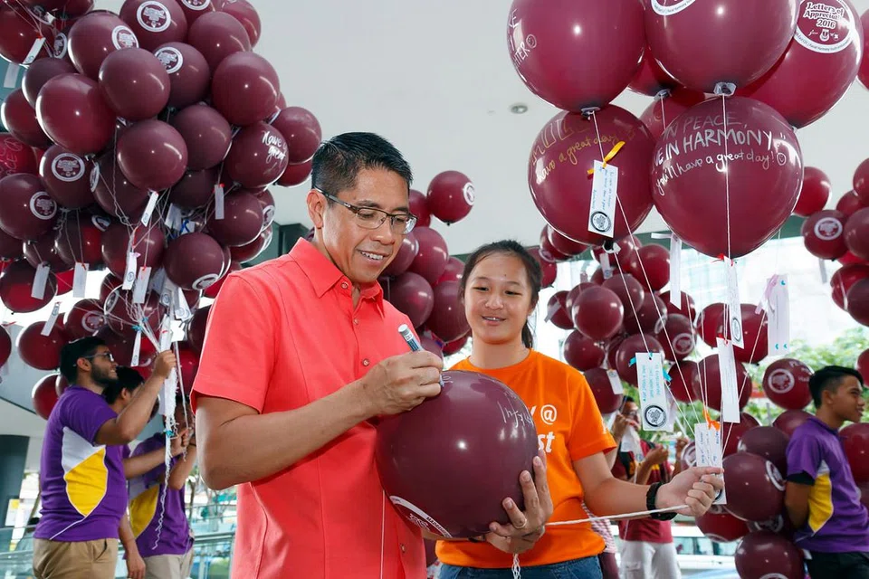 SEBARKAN MESEJ KEHARMONIAN: Dr Maliki mengagihkan belon dengan mesej ucap selamat kepada orang awam di sekitar stesen MRT Paya Lebar, semalam. - Foto CDC SOUTH EAST