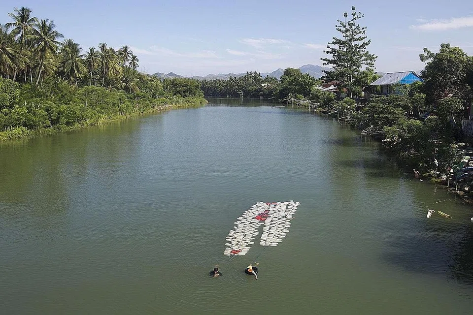 DEMI PENAKATAN: Gambar yang diambil pada 21 Mac ini menunjukkan Hasria (kiri) bersama seorang rakannya berenang balik dengan menarik sekitar 200 bekas berisi air minum buat penduduk kampung mereka di Tinambung, Sulawesi. - Foto AFP