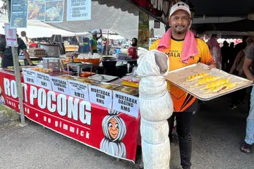 Encik Muhammad Firdaus Kamaruddin, 39 tahun, menunjukkan roti pocong dijualnya di samping replika pocong di gerainya dekat bazar Ramadan Taman Seremban Jaya, Negeri Sembilan.