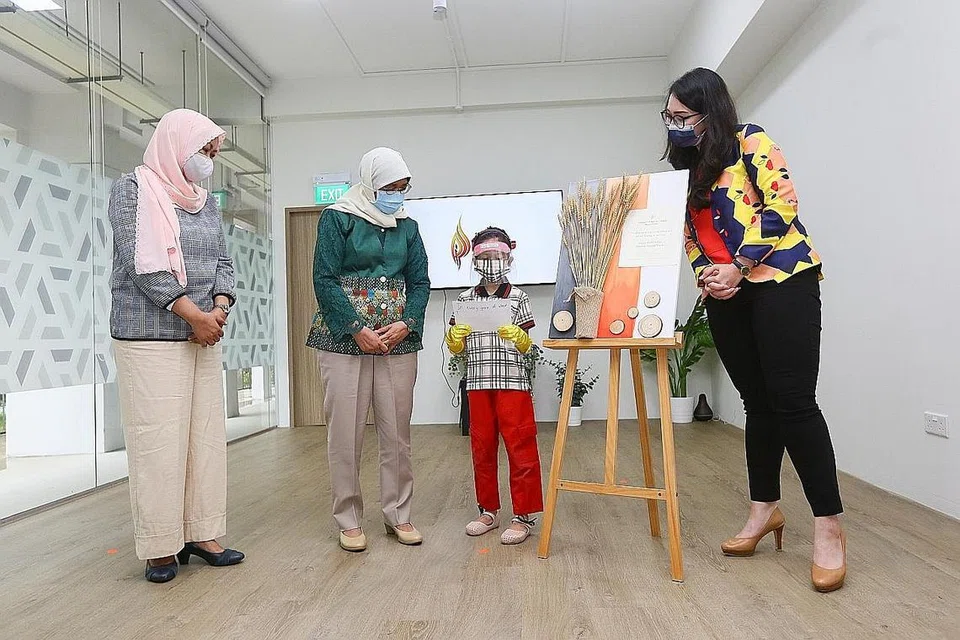 MENJELANG HARI IBU: Pelajar prasekolah PPIS, Dini Eiman Mohamed Hilmi. menyampaikan tanda mata kepada Presiden Halimah Yacob sambil membacakan mesej Hari Ibu. Turut memerhatikan Ketua Pegawai Eksekutif (CEO) PPIS, Cik Tuminah Sapawi (kiri), dan Presiden PPIS, Cik Hazlina Abdul Halim. - Foto ZAOBAO