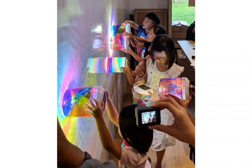 TERPESONA DENGAN HASIL LUKISAN: Kanak-kanak menunjukkan hasil lukisan bekas biskut PET mereka yang akan dipamerkan sebagai pemasangan seni lampu, The Rainbow Connection, di 'i Light Singapore - Bicentennial Edition' tahun depan. - Foto BH oleh ZULAIQAH ABDUL RAHIM