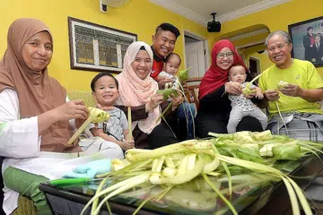 KEKALKAN TRADISI: Keluarga Encik Mohamed Sis (kanan) berusaha mengekalkan tradisi menganyam ketupat dan masak bersama anak, menantu dan kini cucunya. Turut sibuk menganyam ketupat ialah (dari kiri) isterinya Cik Yuhanis Sulaiman, Muhd Naufal Mohd Hairi (cucu), Cik Nur Azzyati (anak), Encik Mohd Hairi Hamssan (menantu), Nur Adawiyah Mohd Hairi (cucu), Cik Norhidayah (anak) dan Emma Maryam Muhd Ramlan (cucu). - Foto KHALID BABA