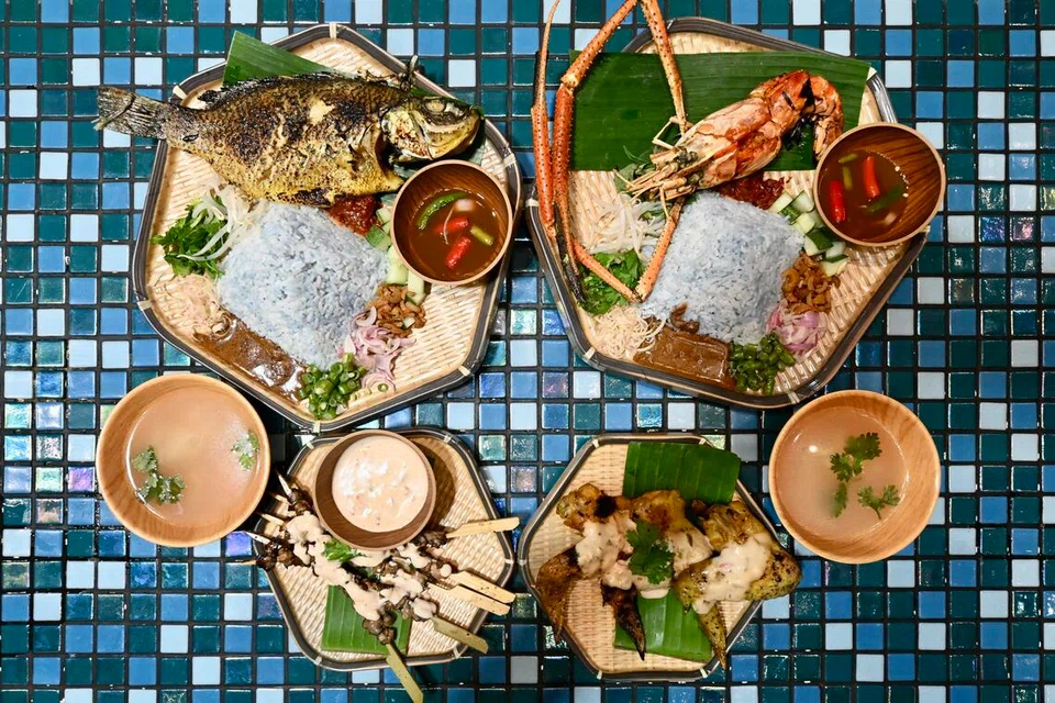 (dari kiri) Hidangan Asam Picit Ikan Bakar, $14 dan Udang Bakar, $16 disertakan dengan nasi ulam, sambal ikan kurau masin dan kaldu ayam. Hidangan sampingan ialah ayam percik Kelantan, $7 dan sate kerang bakar pecel, $6 yang disertakan dengan sos pecel.