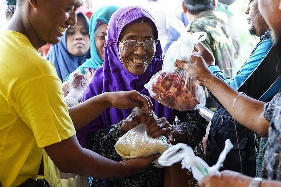 KEBAHAGIAAN TERPANCAR: Seorang penduduk desa dari gunung turun ke stadium Plumbon Pasuruan, Indonesia, untuk menerima sumbangan daging korban dan beras anjuran IbadahSg. - Foto IBADAHSG PTE LTD