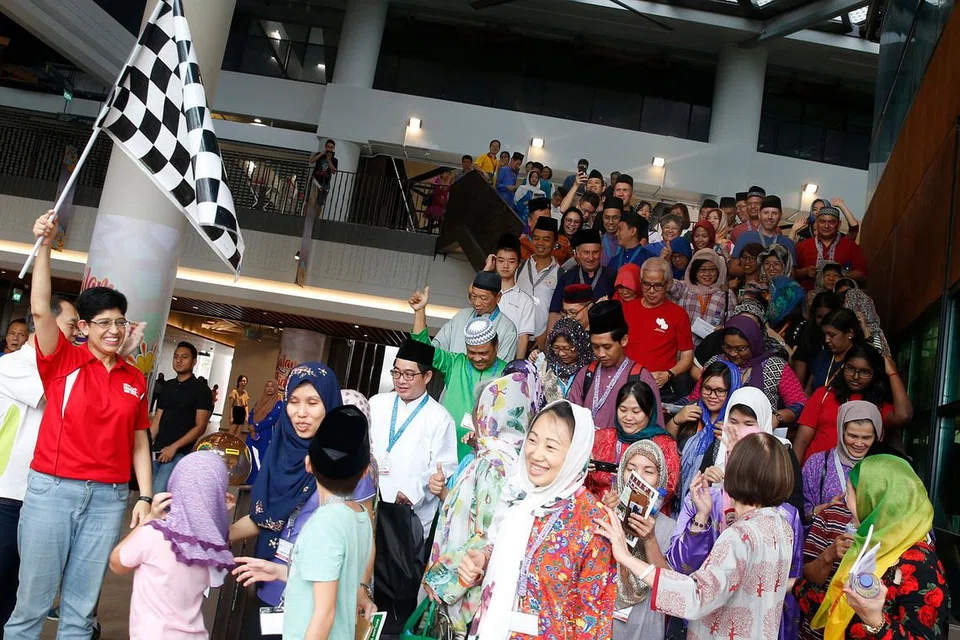 BERSEMANGAT UNTUK BERLUMBA: Peserta, yang kebanyakannya bukan berbangsa Melayu, mengenakan pakaian Melayu dalam perlumbaan warisan budaya untuk mempelajari tentang budaya Melayu. AP GRC Marine Parade, Profesor Madya Fatimah Lateef (kiri, berbaju merah) mengibarkan bendera sebagai tanda permulaan perlumbaan tersebut. - Foto BH oleh TIMOTHY DAVID