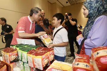 Menteri Negara (Ehwal Dalam Negeri merangkap Pembangunan Negara), Profesor Madya Dr Muhammad Faishal Ibrahim (kiri), mengagihkan barangan keperluan kepada seorang penerima dalam acara ABS Community Marketplace sempena pelancaran majlis Program Menyumbang Kembali oleh Masyarakat Persatuan Bank Singapura (ABS) di HomeTeamNS Khatib Clubhouse pada 8 Jun. Majlis tersebut diadakan sebagai sebahagian daripada pelancaran kempen #GiveAsOneSG Perbarisan Hari Kebangsaan (NDP) 2024.