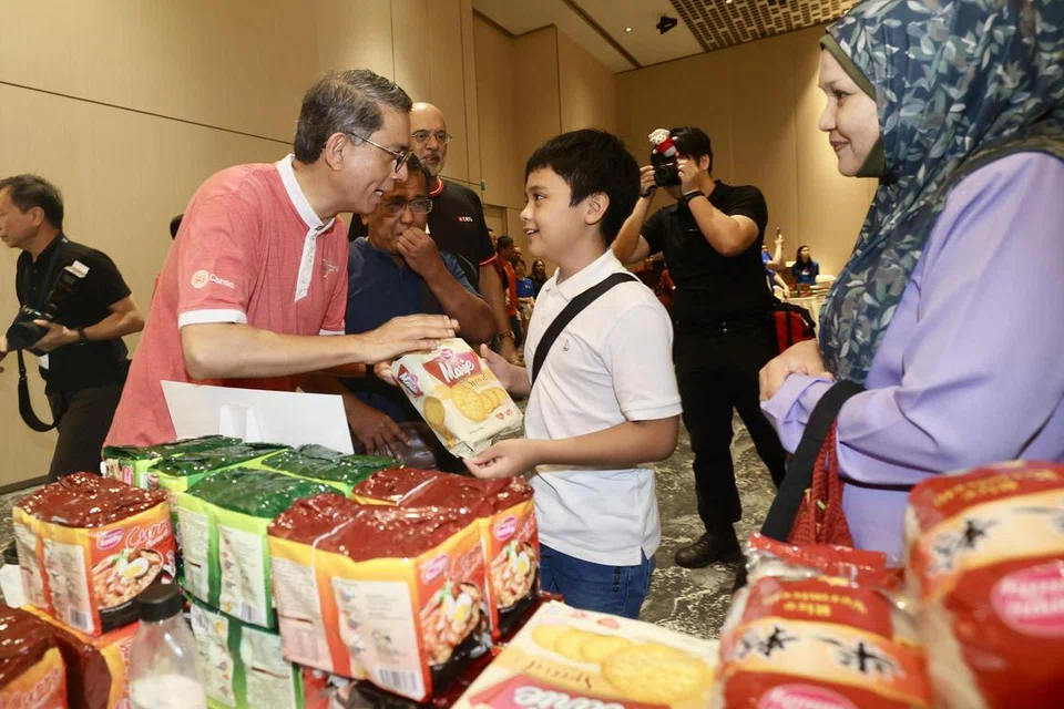 Menteri Negara (Ehwal Dalam Negeri merangkap Pembangunan Negara), Profesor Madya Dr Muhammad Faishal Ibrahim (kiri), mengagihkan barangan keperluan kepada seorang penerima dalam acara ABS Community Marketplace sempena pelancaran majlis Program Menyumbang Kembali oleh Masyarakat Persatuan Bank Singapura (ABS) di HomeTeamNS Khatib Clubhouse pada 8 Jun. Majlis tersebut diadakan sebagai sebahagian daripada pelancaran kempen #GiveAsOneSG Perbarisan Hari Kebangsaan (NDP) 2024.