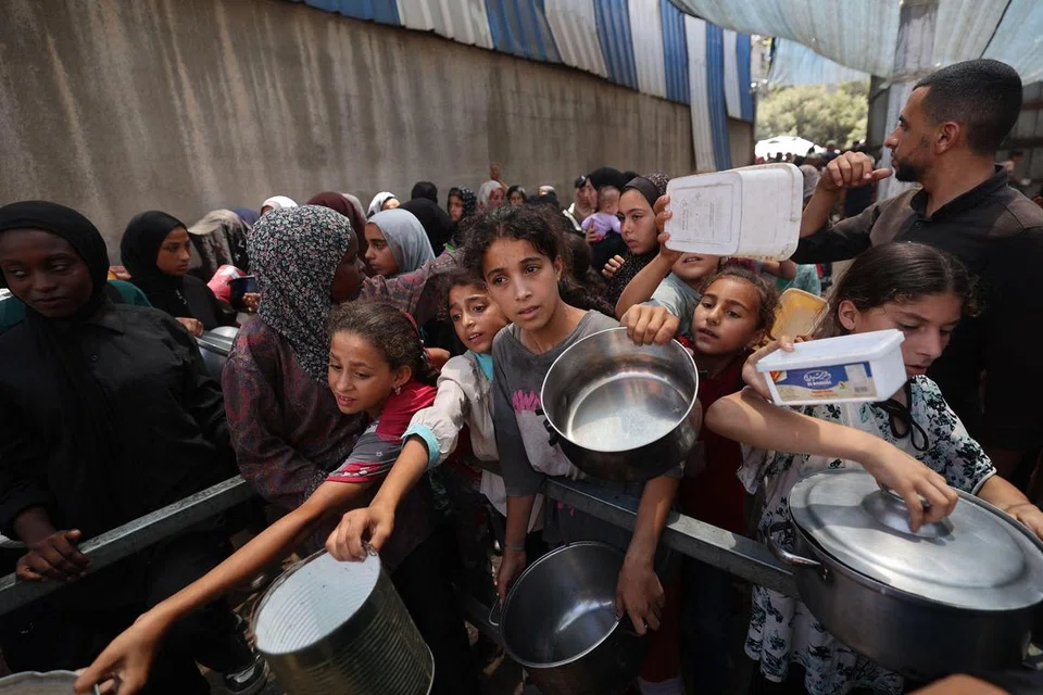 Kanak-kanak Palestin beratur untuk mendapatkan sebahagian makanan panas yang diagihkan oleh dapur amal di kem pelarian Nuseirat di tengah Jaluran Gaza pada 15 Julai 2025