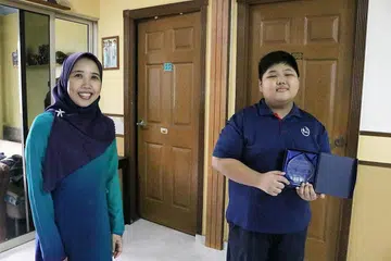 TUNJUK KEMAJUAN BAIK: Timbalan Ketua Pegawai Eksekutif (CEO) Cik Aidaroyani Adam menyampaikan plak pencapaian kepada Zachary yang meraih anugerah Pelajar Keseluruhan Terbaik (Kategori PSLE). - Foto YAYASAN MENDAKI