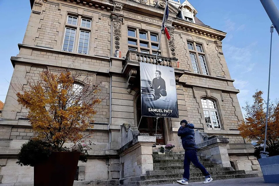 PADAH TINDAKAN MELAMPAU: Seorang pejalan kaki melepasi luar bangunan Dewan Bandaraya di Conflans-Sainte-Honorine, 30km dari barat laut Paris, pada 3 November lalu, yang memaparkan kain rentang dihiasi wajah guru warga Perancis, mendiang Encik Samuel Paty, menyusuli tindakan pengganas memenggal kepalanya pada 16 Oktober lalu kerana memaparkan wajah Nabi Muhammad saw dalam bentuk kartun. - Foto AFP