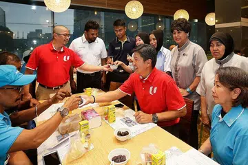 BERBUKA BERSAMA: Encik Zainal Sapari (kiri, baju merah) dan Encik Ng Chee Meng (duduk, baju merah) berbuka puasa dengan sekitar 60 pekerja pembersihan, kawalan perosak dan landskap di Asia Square Tower 2 kelmarin menyusuli satu majlis menandatangani MOU bagi Batu dan Cleaning Express membentukkan Jawatankuasa Latihan Syarikat. - Foto ROSLEE ABDUL RAZAK