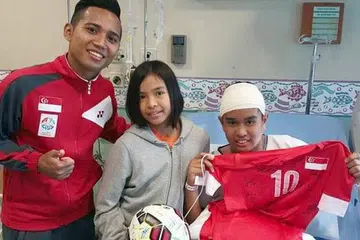 KEJUTAN MANIS: Murid Sekolah Rendah Tanjong Katong Emyr Uzayr begitu gembira sekali apabila pemain bola sepak kegemarannya, Sahil Suhaimi, datang mengunjunginya. Bersama mereka ialah adik Emyr. - Foto FACEBOOK