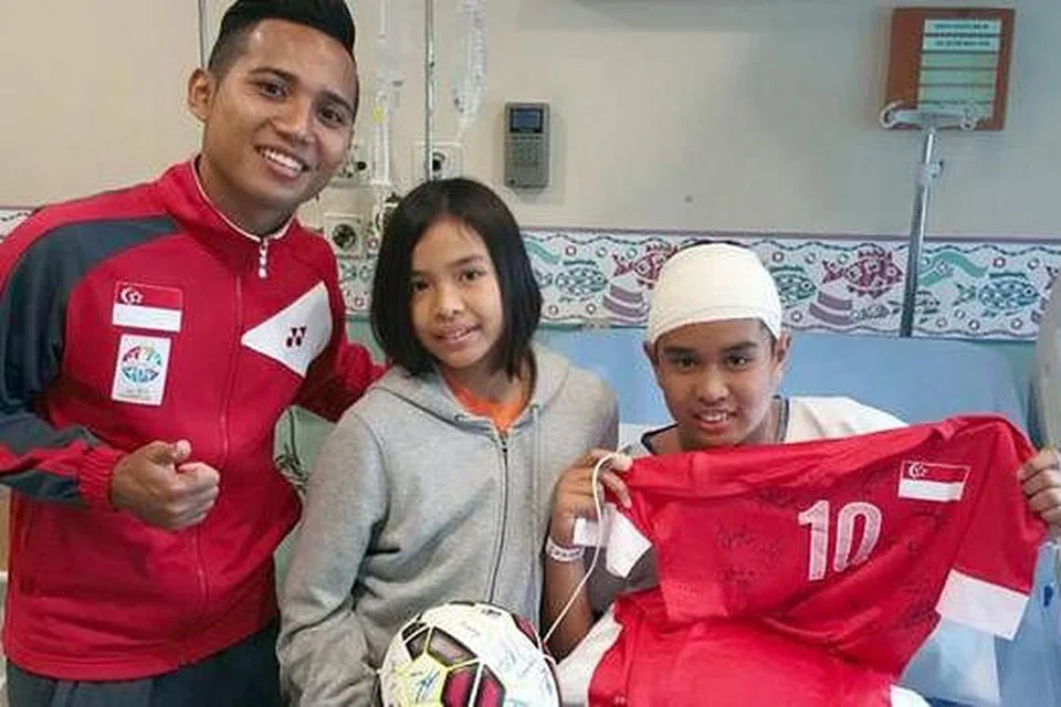 KEJUTAN MANIS: Murid Sekolah Rendah Tanjong Katong Emyr Uzayr begitu gembira sekali apabila pemain bola sepak kegemarannya, Sahil Suhaimi, datang mengunjunginya. Bersama mereka ialah adik Emyr. - Foto FACEBOOK