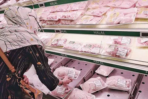 BELI AYAM: Seorang wanita dilihat di NTUC FairPrice di Woodlands memilih ayam segar untuk dibeli.
