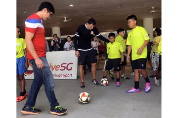 DILATIH IKON BOLA SEPAK: Dua beradik, Muhammad Dzulhelmy Muhammad Halil (kanan) dan adiknya, Muhammad Dzulhelfy (dua dari kanan), menyertai program CDC North East dan Akademi Bola Sepak ActiveSG sejak November tahun lalu. Mereka kelihatan menendang bola sepak bersama Mayor CDC North East, Encik Teo Ser Luck (kiri), dan Pengetua Akademi Bola Sepak ActiveSG, Aleksandar Duric (tengah). - Foto KHALID BABA