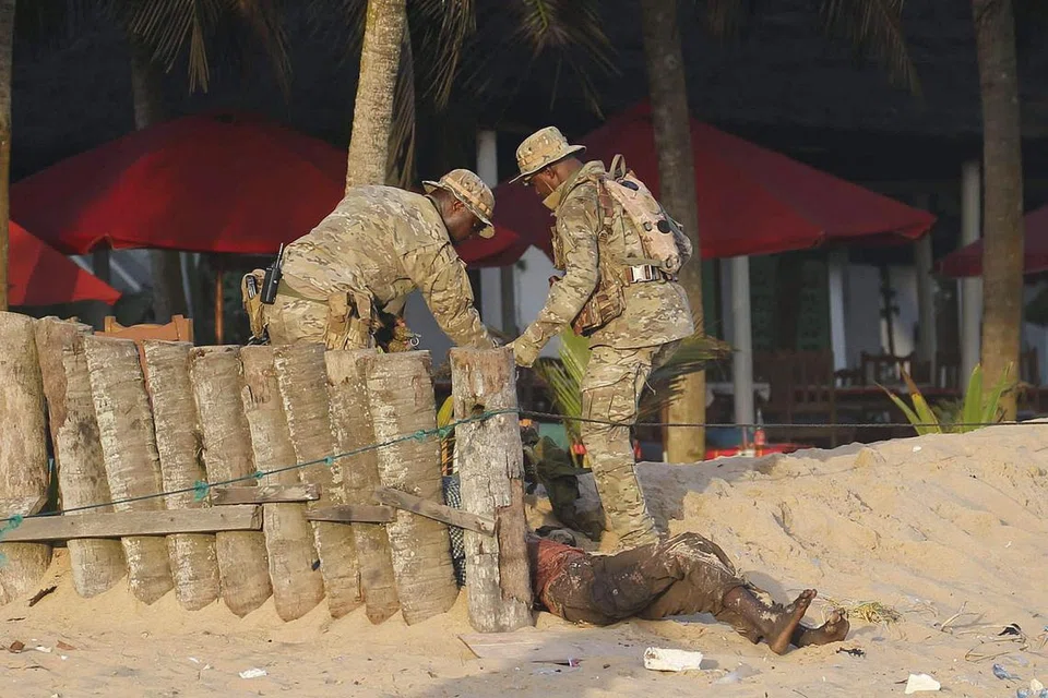 PERIKSA MAYAT: Pegawai keselamatan memerika mayat seorang mangsa di pantai di Grand Bassam. -- Foto REUTERS