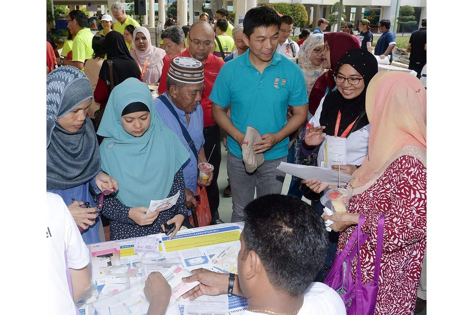 MEMERIKSA KESIHATAN: Encik Tan (empat dari kanan) berbual-bual dengan penduduk yang mengunjungi gerai Persatuan Barah Singapura yang terdapat di Karnival@461. - Foto TAUFIK A. KADER.