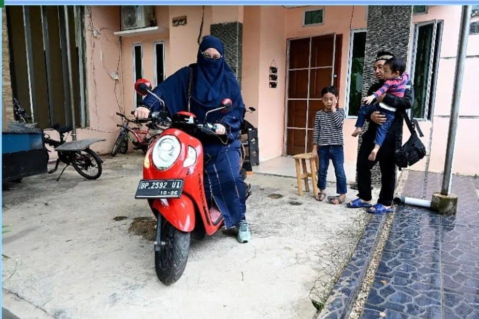 Cik Nur Asyiqin Jumuto, warga Singapura, menaiki motosikal untuk ke kilang jahitnya di Batam Centre diperhatikan oleh suaminya Encik Ahmadi Yuswar, seorang warga Indonesia juga seorang peniaga, serta dua anak mereka.