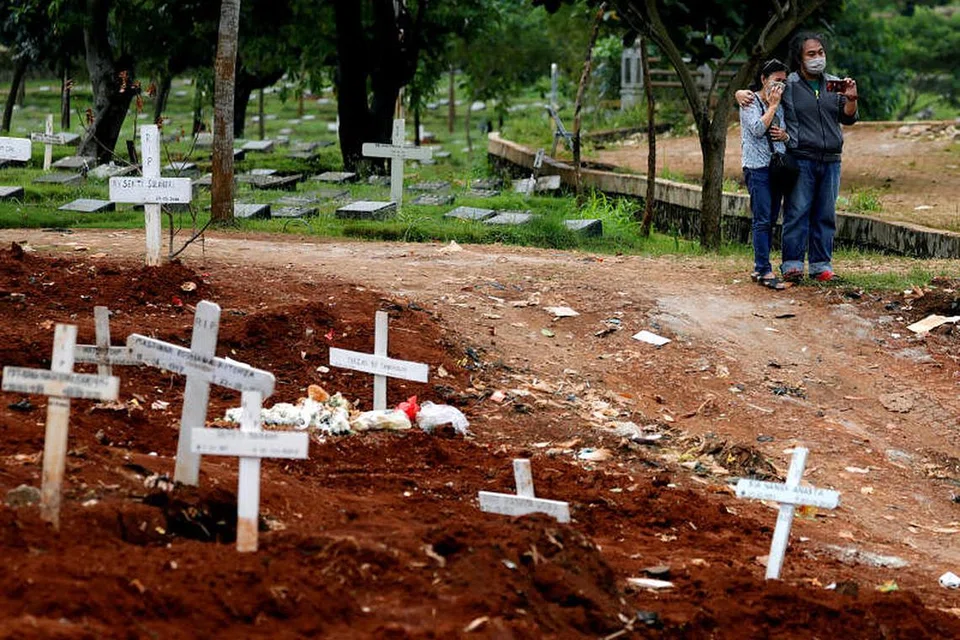 KORBAN AKIBAT VIRUS: Foto fail menunjukkan ahli keluarga memakai pelitup semasa mengunjungi pusara mangsa jangkitan Covid-19. 