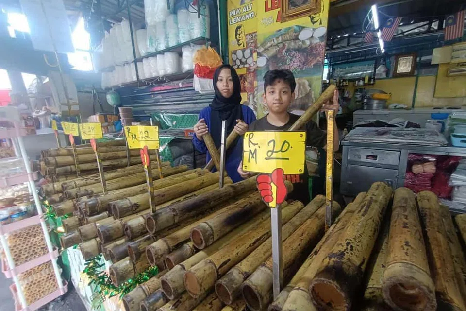 Dua anak Cik Badriah Najib Hasbi, pemilik kedai Lemang Pak Ali di Hulu Klang, Selangor, menunjukkan variasi saiz dan harga lemang yang dijual di kedai mereka.