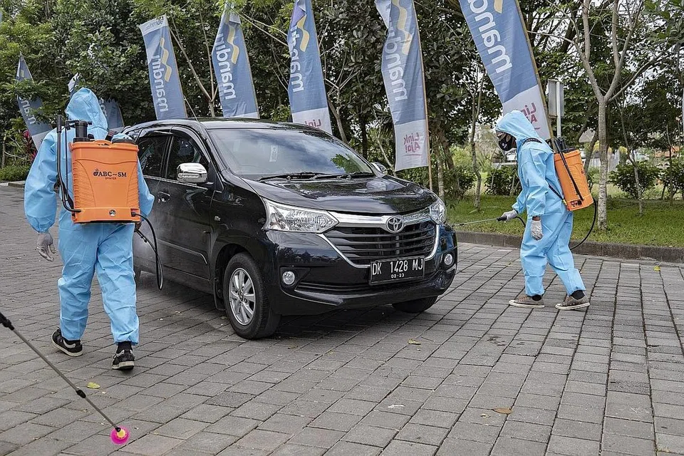 LANGKAH SELAMAT: Dua pekerja menyembur bahan penyahjangkit pada kereta sebelum dibenarkan masuk bagi satu acara di Ubud, Bali, yang telah dibuka semula bagi pelancong domestik. - Foto EPA-EFE