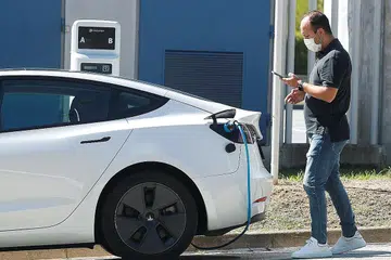 BERSAMA TANGANI PEMANASAN GLOBAL: Seorang lelaki memeriksa telefon bimbit sementara beliau mengecas kereta elektrik Tesla di Sant Cugat del Valles, berdekatan Barcelona, Sepanyol. - Foto REUTERS