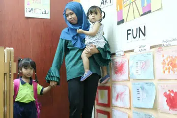 ULANG-ALIK KE SEKOLAH: Cik Nur Diyana Taha menghantar anak sulungnya, Haifa Daniya Mohammad Haarifan, sekitar 9 pagi dan mengambilnya pulang sekitar 6.30 petang setiap hari. Anak keduanya Hilya Dahlia (didukung) pula akan diletakkan di rumah ibu mentuanya. - Foto SHAKIR SAIFUDDIN
