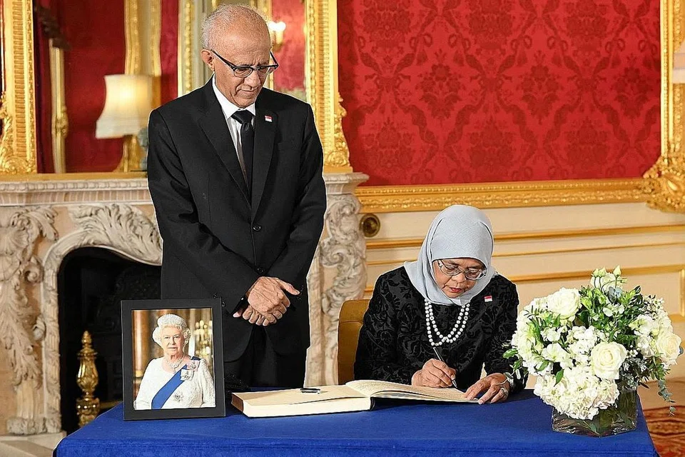 UCAP TAKZIAH: Presiden Halimah, diiringi suaminya, Encik Mohamed Abdullah Alhabshee, menandatangani buku takziah di Lancaster House semasa lawatannya ke London. - Foto AFP