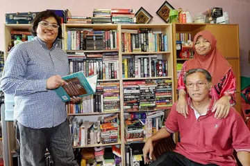 TANAM MINAT SUKA MEMBACA: Encik Suhaiemi Sakon dan Cik Khalijah Hassan (kanan) membiasakan anak dengan buku sejak kecil. Tabiat membaca membolehkan kesemua anak mereka, termasuk Cik Tuty Norashikin (kiri), mencapai kejayaan cemerlang dalam pelajaran. - Foto ZAINAL YAHYA.
