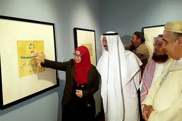 BERI PENERANGAN: Cik A'tii Qah sedang memberi penerangan kepada tetamu terhormat Encik Mohammed Al Murr (berjubah putih) tentang seni khat Islam yang dihasilkannya. - Foto ihsan A'TII QAH SUHAIMI