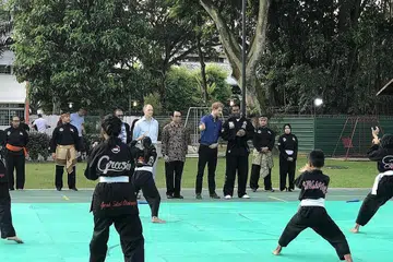 PELAJARI BUDAYA MELAYU: Putera Harry (berbaju biru) menyaksikan demonstrasi silat sambil diterangkan tentang seni silat oleh Sheik Alauddin. - Foto SITI AISYAH NORDIN