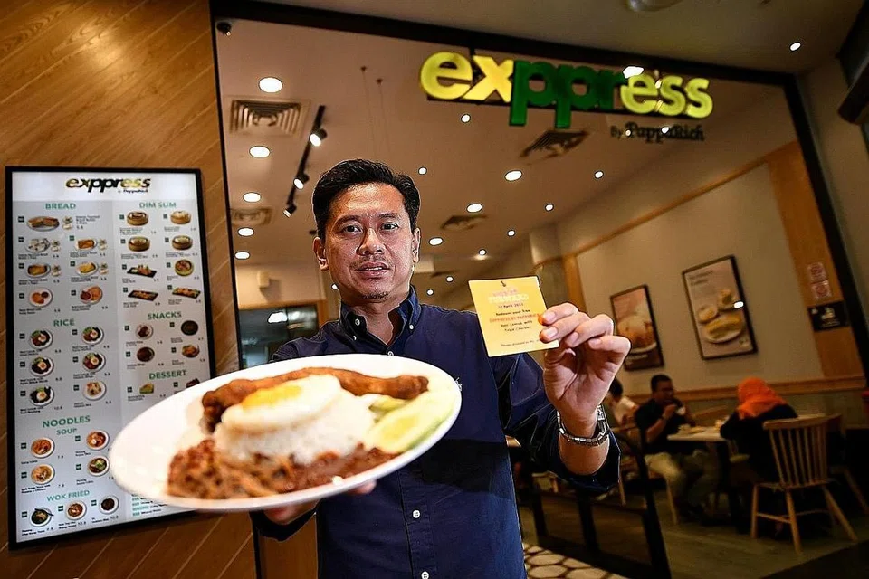 GUNA KUPON: Di Restoran Express by Papparich, kupon yang diberi kepada penerima tajaan boleh ditukar dengan sajian makanan 'signature' mereka, nasi lemak dengan peha ayam yang ditunjukkan oleh Ketua Eksekutif (Rantau Asia), Encik Sebastian Low.