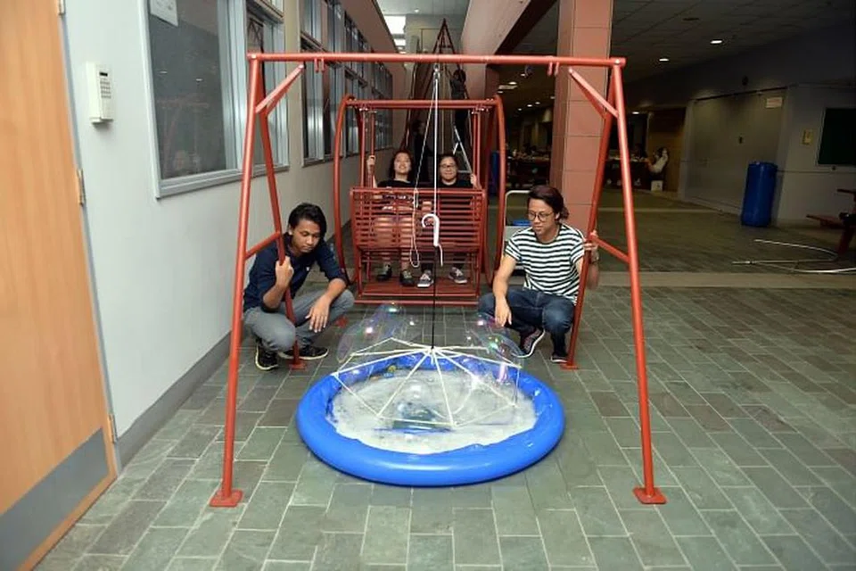 HASIL GELEMBUNG SABUN: Pengunjung boleh cuba menghasilkan gelembung sabun untuk menangkap cahaya apabila mereka duduk di kerusi berayun dan turbin bergelembung bagi seni pemasangan Clockwork Stories rekaan penuntut Politeknik Nanyang. Encik Muhammad Khuraihan Amron (kiri) dan Encik Muhammad Mirza Ramlan (kanan) kelihatan bersama anggota kumpulan lain.
