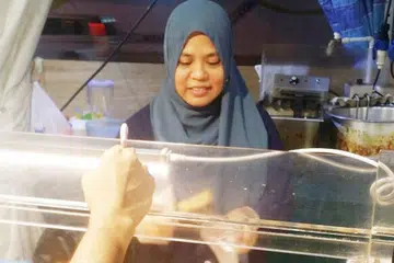PASAR MALAM JADI SUMBER REZEKI: Cik Munah (gambar atas) berjualan makanan seperti burger dan keropok lekor di pasar malam sejak 15 tahun lalu. Beliau dibantu adik angkatnya, Encik Mohd Ridzuan, sejak tujuh tahun lalu. - Foto-foto ihsan MOHD RIDZUAN MOHD SENIN dan SHAHRIYA YAHAYA