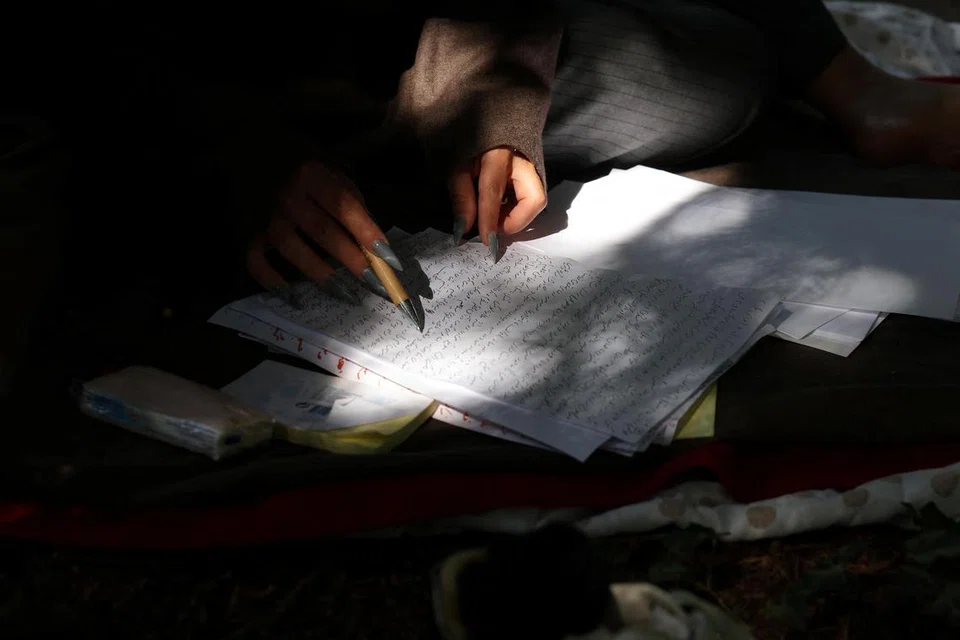 Nadia Feyzi, 32 tahun, seorang artis Afghanistan yang  berhijrah ke Jerman, membaca semula halaman manuskripnya yang baru sahaja selesai ditulisnya semasa duduk di tanah perkuburan yang dia pergi untuk mendapatkan inspirasi di Bonn, Jerman, 15 Julai 2025 (Foto hiasan).