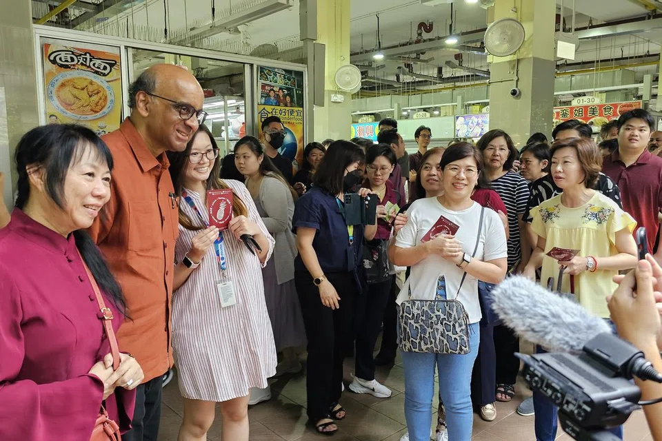 BERATUR PANJANG: Pengunjung di Pusat Makanan Amoy Street di Maxwell Road beratur panjang untuk mengambil giliran bergambar bersama calon Presiden Encik Tharman Shanmugaratnam (dua dari kiri) dan isterinya Cik Jane Yumiko Ittogi (paling kiri) semasa waktu makan tengah hari pada Jumaat.