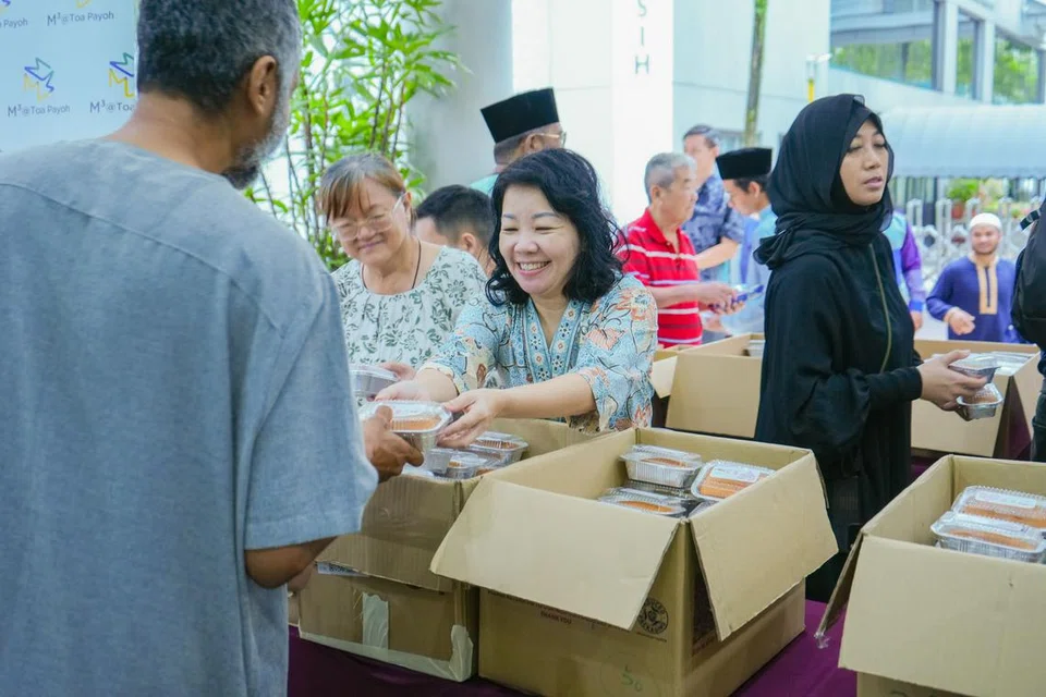 Sukarelawan Jawatankuasa Eksekutif Kegiatan Melayu (MAEC) Toa Payoh West-Thomson (TWT), Cik Cindy Chia (dua dari kanan), mengedarkan kek mentega dibakarnya kepada jemaah Masjid Muhajirin pada 31 Mac, iaitu hari pertama Syawal.