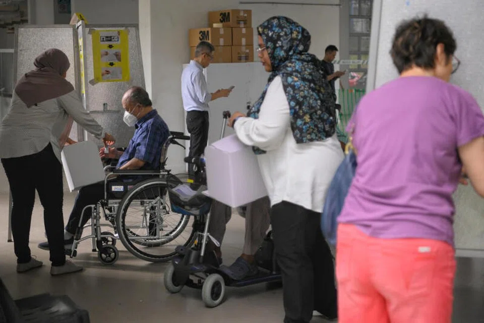 LALUAN KHAS: Pegawai pilihan raya membantu seorang pengundi berkerusi roda di pusat mengundi di kolong Blok 307 Jurong East Street 32.