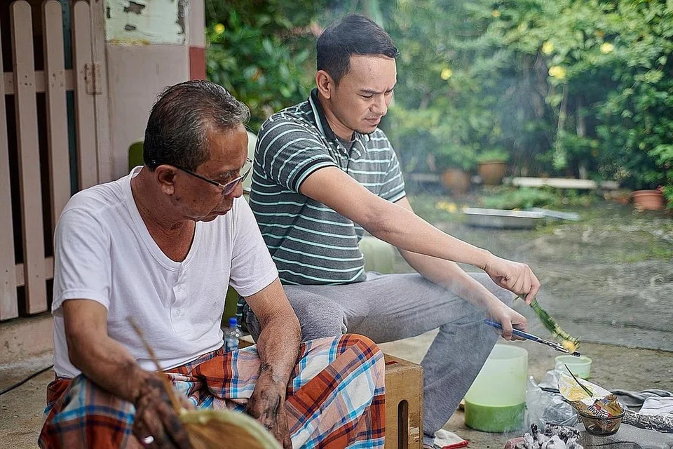 SERONOK BEREKSPERIMEN: Norman Ishak (kanan) yang menjayakan filem pendek 'Arang' teruja siapkan kuih bakar dengan menggunakan arang di Kampung Buangkok. - Foto ESPLANADE 