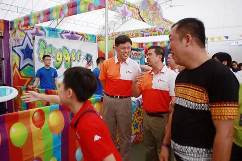 BANTUAN UNTUK MEMERLUKAN: Encik Chan (tengah, kiri) bersama Encik Zainal (tengah, kanan), yang hadir di Karnival Keluarga Riadah dan Seronok di Downtown East, mengumumkan lebih ramai anggota memerlukan layak menerima program baucar NTUC. - Foto THE STRAITS TIMES