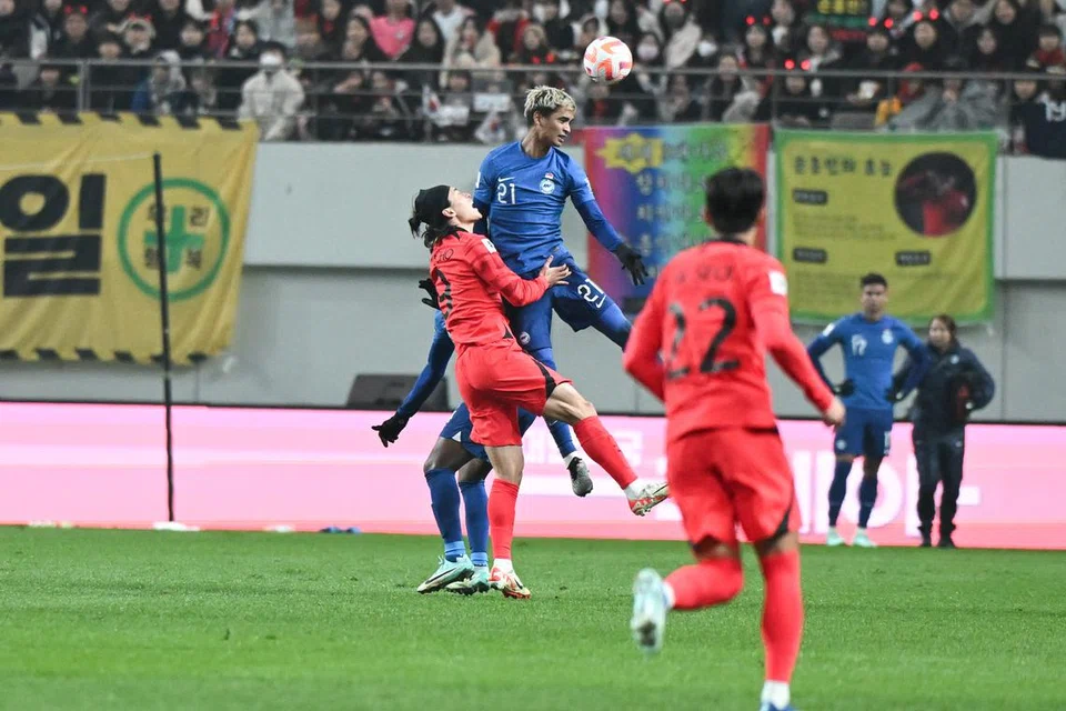 MENCABAR: Pemain pertahanan Singapura, Safuwan Baharudin (tengah, jersi biru) melompat tinggi untuk menanduk bola menentang penyerang Korea Selatan, Cho Geu-sung dalam aksi pembukaan pusingan kedua Kelayakan Piala Dunia di Stadium Piala Dunia Seoul pada Khamis. 
