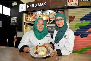 NIAGA NASI LEMAK: Cik Raihanah Mohd Halim (kiri) kini seronok berjualan nasi lemak setelah diberi tanggungjawab oleh ibunya, Cik Rohaniah Mohamed (kanan), dengan menubuhkan dan mengendalikan perniagaan nasi lemak milik syarikat keluarganya. - Foto M.O. SALLEH