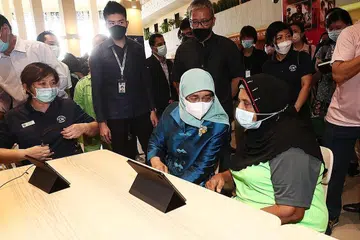 PERANTI IM-OK: Cik Khatihah, 81 tahun menunjukkan aplikasi yang seringkali digunakannya di dalam alat peranti IM-OK kepada Puan Halimah Yakob. - Foto BM oleh KELVIN CHNG